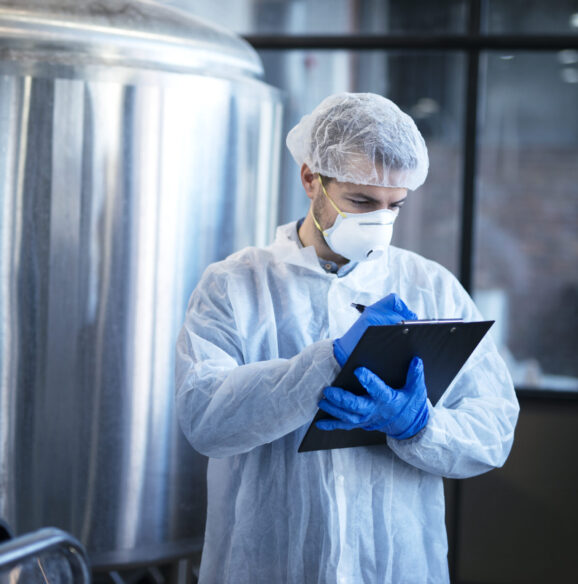Concentrated technologist expert in white suit controlling production in food factory.